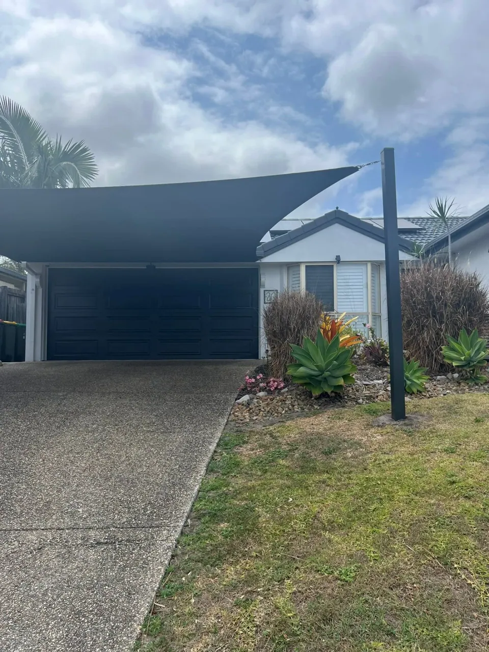 A custom sail and dark posts alongside a landscaped front garden.