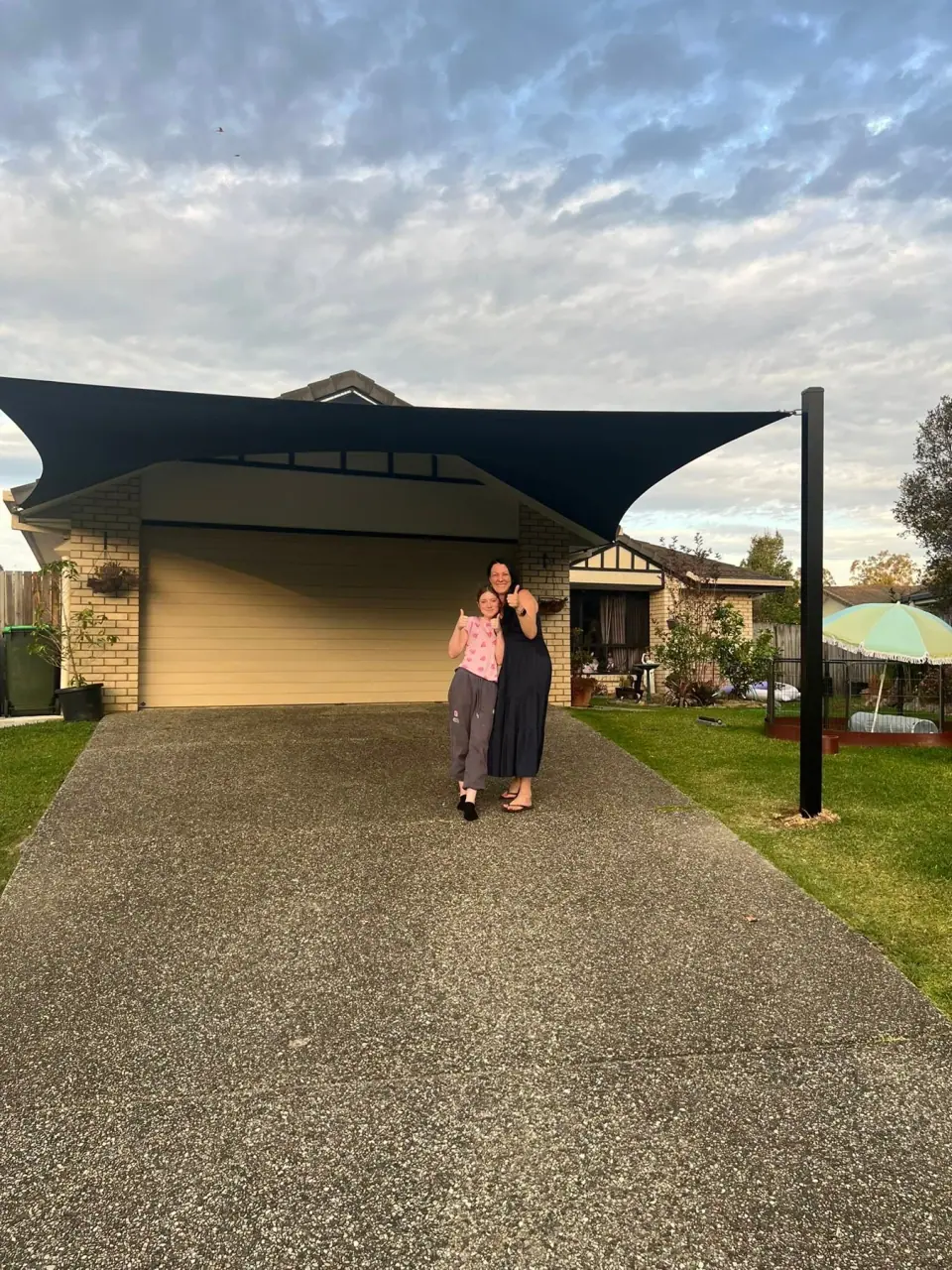 A completed carport shade sail in front of a brick home.